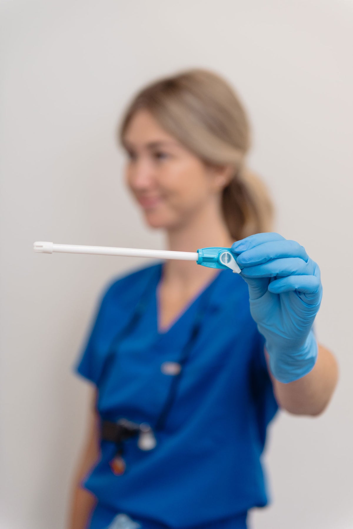 A healthcare worker in blue scrubs holds a blue dental device, photographed against a soft, light gray background with the person intentionally blurred.