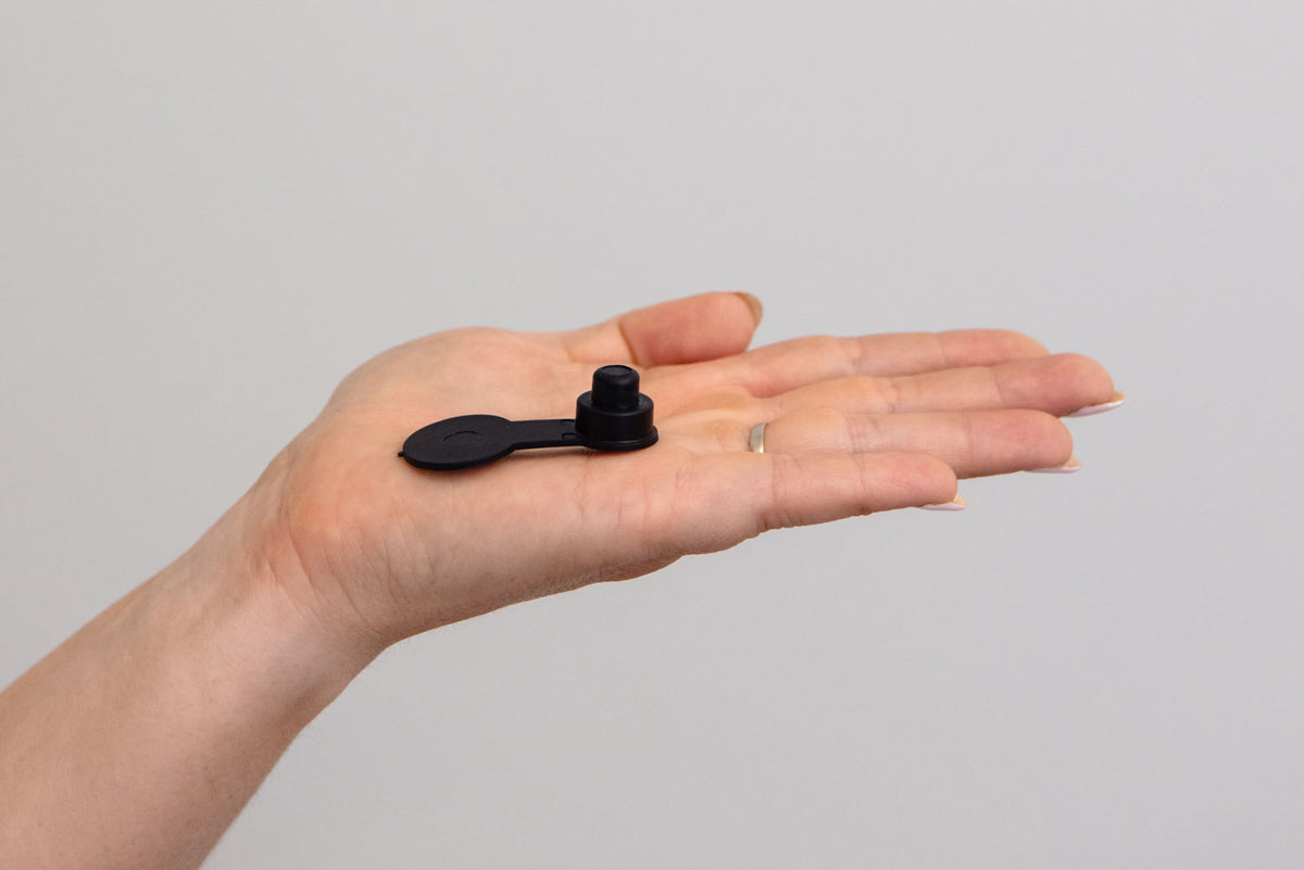 A small black plastic tailcamp with a flat tab, shown resting on an open hand against a plain light gray background.